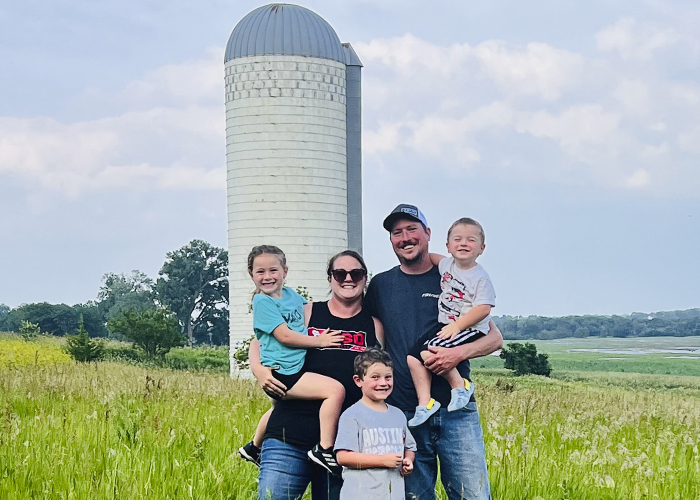 Five people standing in a field in front of a silo
