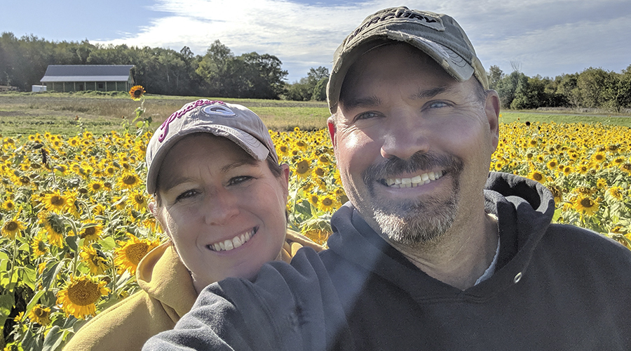 Two people standing in field of sunflowers