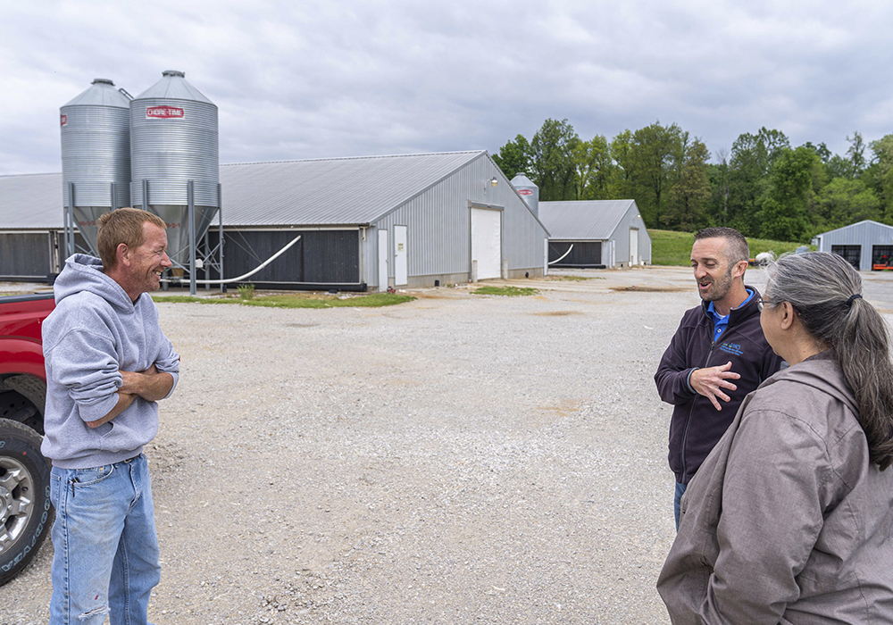 Three people talking in driveway of feed buildings