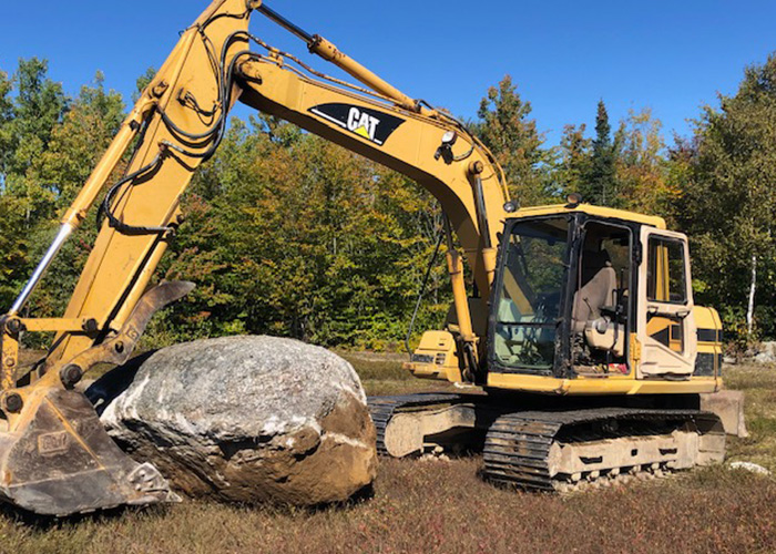 Back hoe picking up boulder