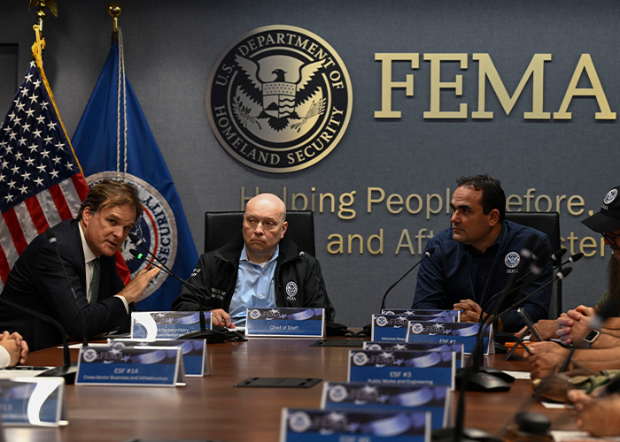 Three people sitting at table in front of FEMA signage on wall