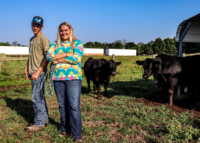 Two people standing in a pasture with two cows