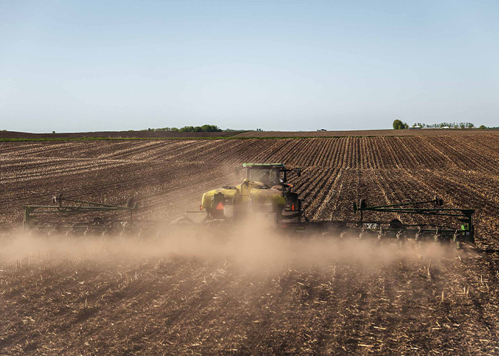 Tractor plowing field in plum of dust