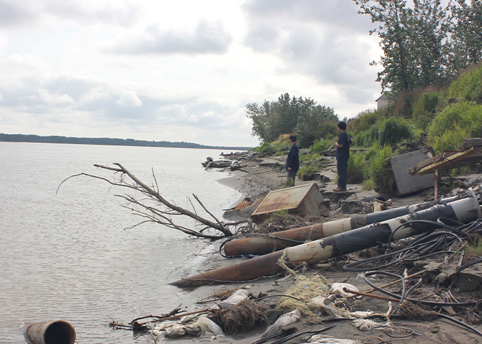 Two people standing on debris on the bank of a river