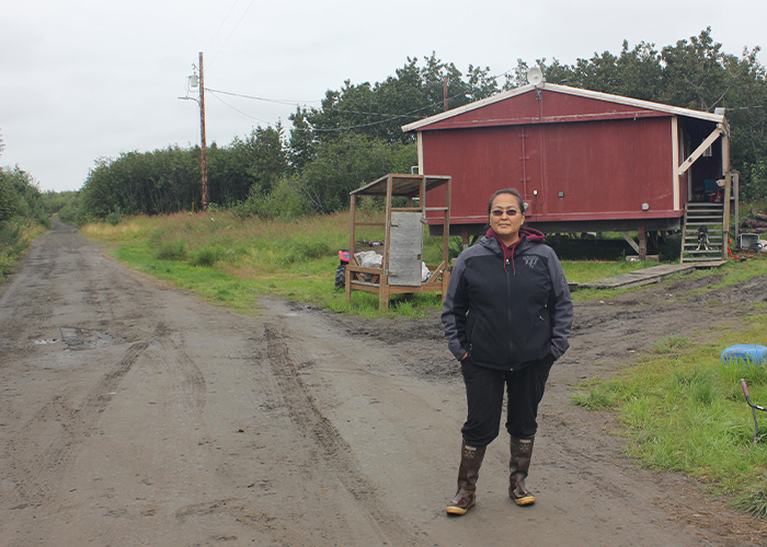 Person standing on a dirt road in front of a red building