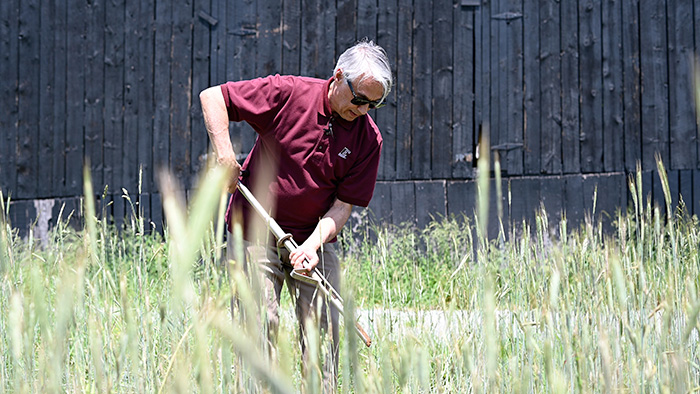 Person using soil monitoring tool in field by a barn