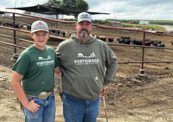 Two people standing next to a fence with cows in the background